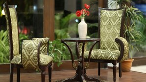 Une pièce avec une table ronde en bois, deux fauteuils à motifs et un vase rempli de fleurs rouges.