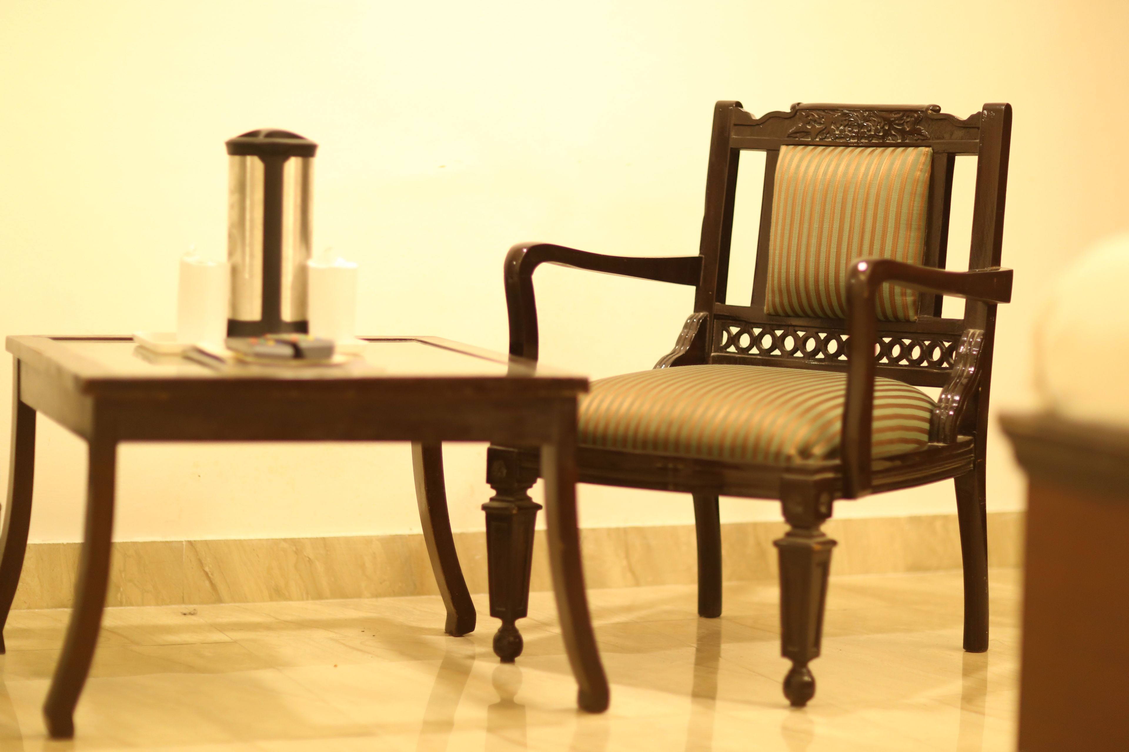 A wooden chair with a cushioned seat and backrest, positioned next to a small table with a cylindrical object on it.