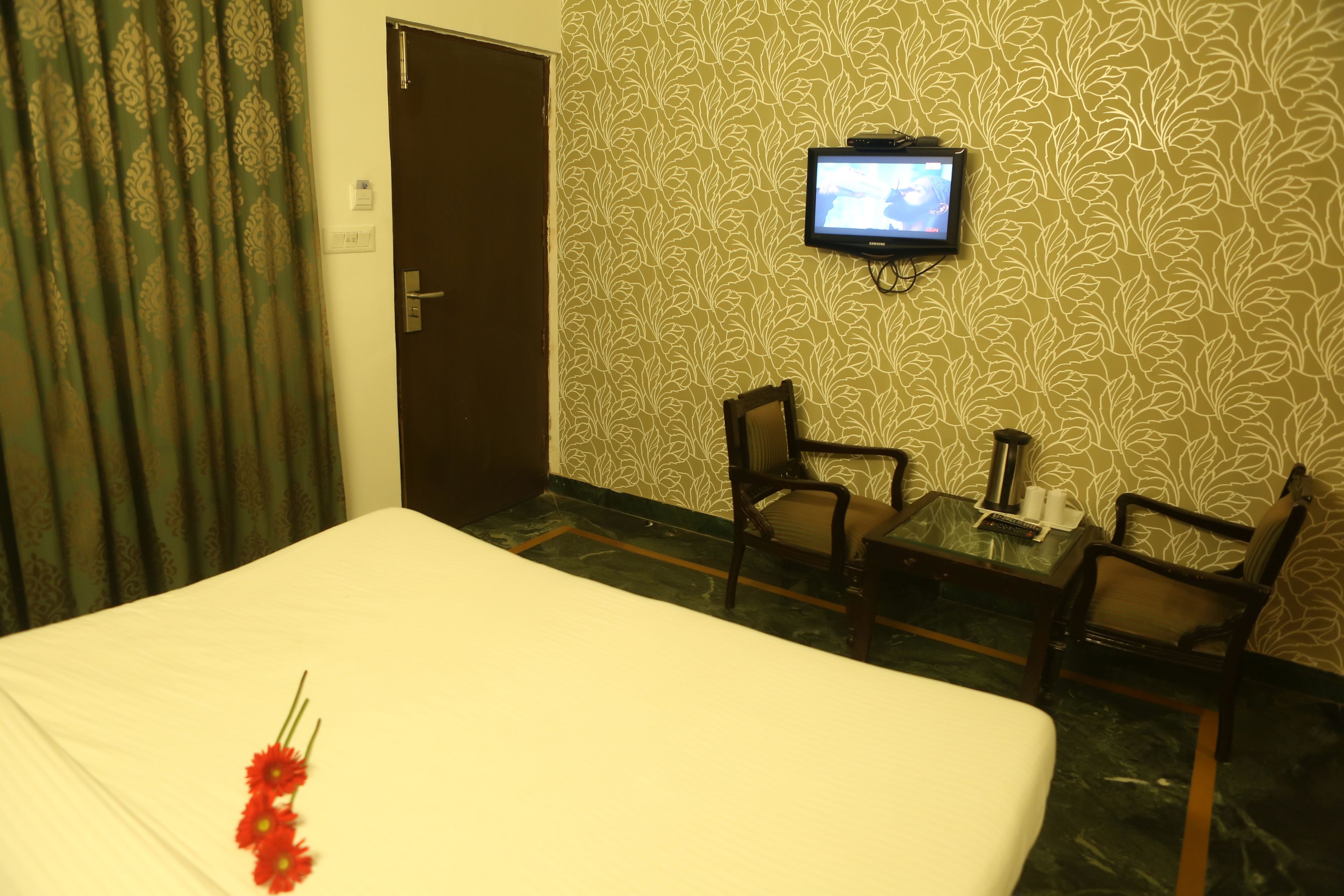 Une chambre d’hôtel avec un lit, deux chaises, une petite table, un téléviseur et un mur décoré de motifs.