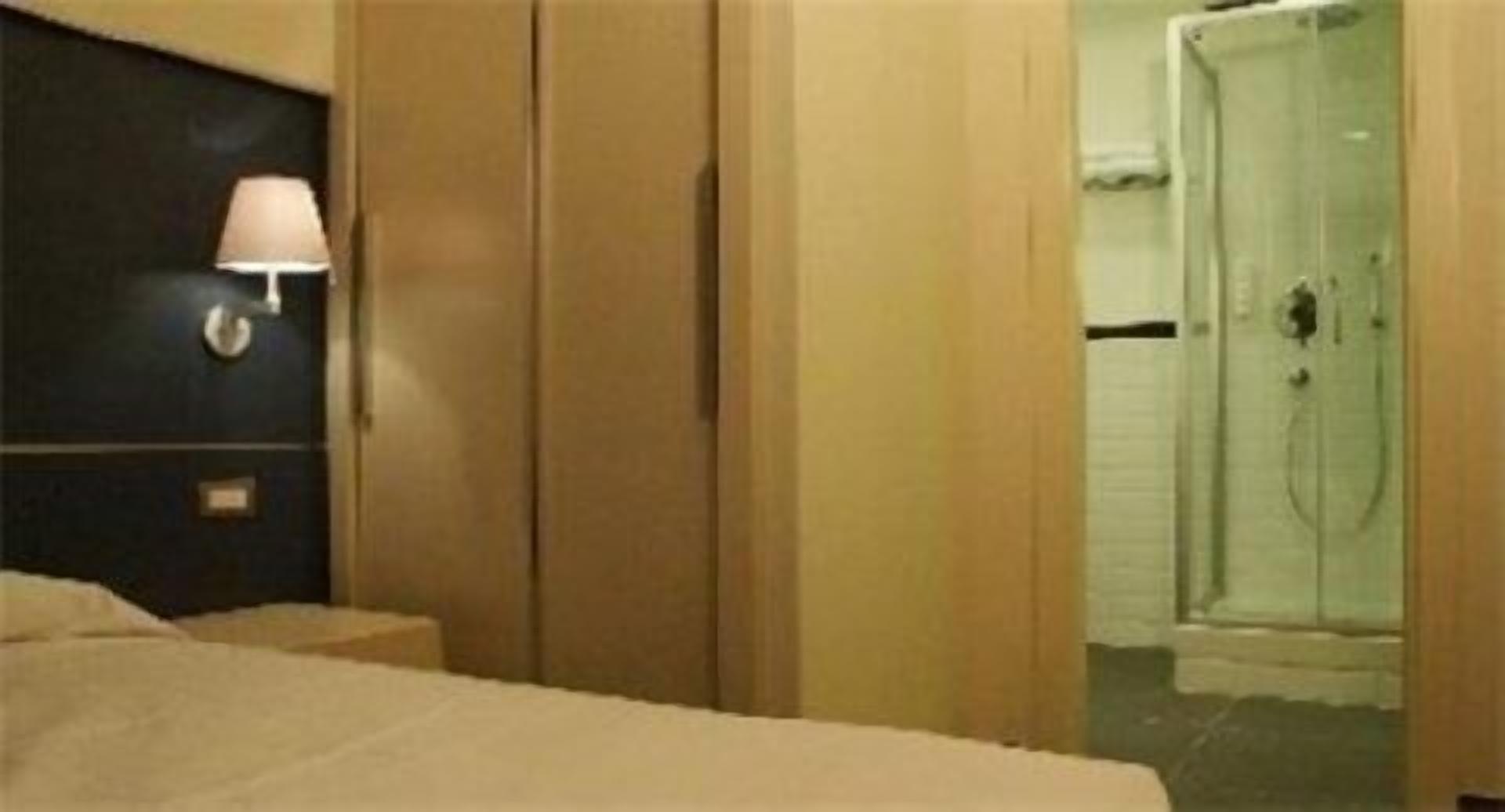 Una habitación de hotel con una cama, una mesita de noche, una lámpara y una puerta que da a un baño.