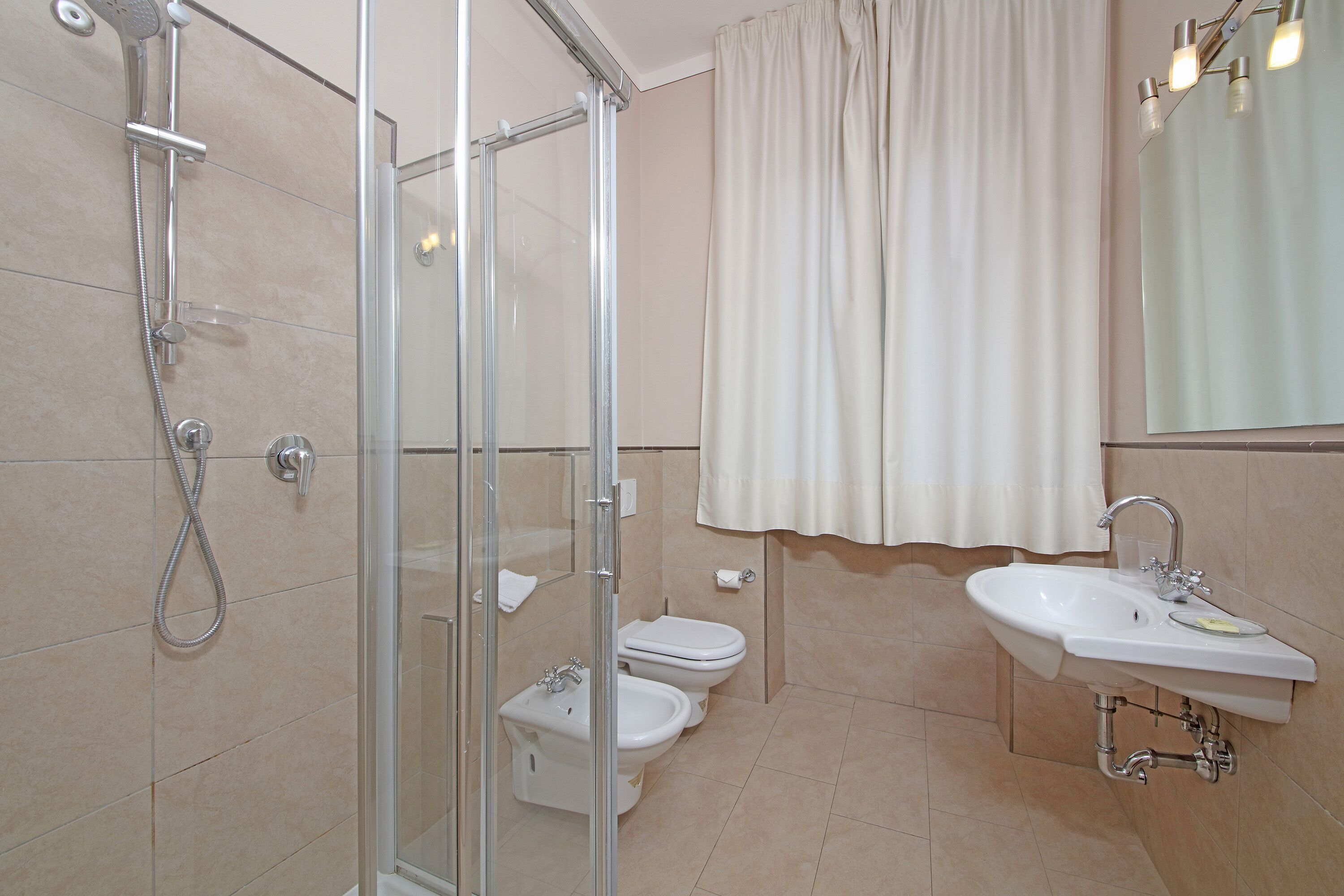 Un bagno moderno con doccia vetrata, due servizi igienici e un lavabo con specchio sopra.