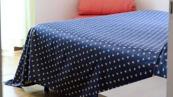 Un dormitorio con una cama, un almohadón rojo, una colcha azul con estampado y un cuadro en la pared.
