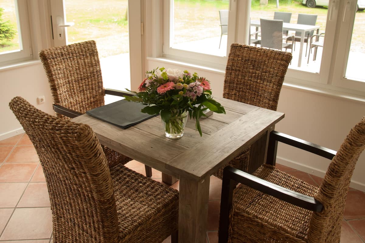 A dining area with a wooden table, wicker chairs, and a vase of flowers.