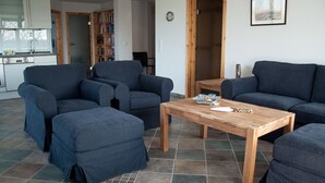 A living room with a sofa set, a wooden coffee table, and a kitchen area in the background. - urlaubsart - Guldehof (Stoltebuell)