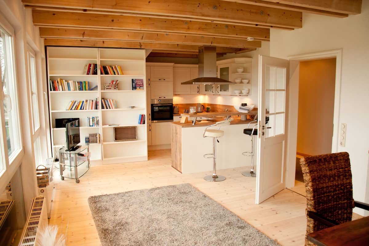 A spacious kitchen with wooden beams, white cabinetry, and a central island with bar stools.