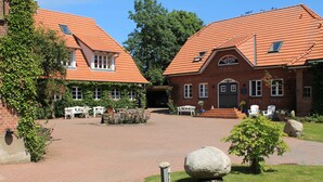 A courtyard with brick pathways, stone bollards, and a small garden area with a tree and a bench. - urlaubsart - Guldehof (Stoltebuell)