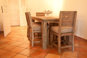 Ein Essbereich mit einem Holztisch und vier Stühlen, eine weiße Tür im Hintergrund und ein gefliester Boden.