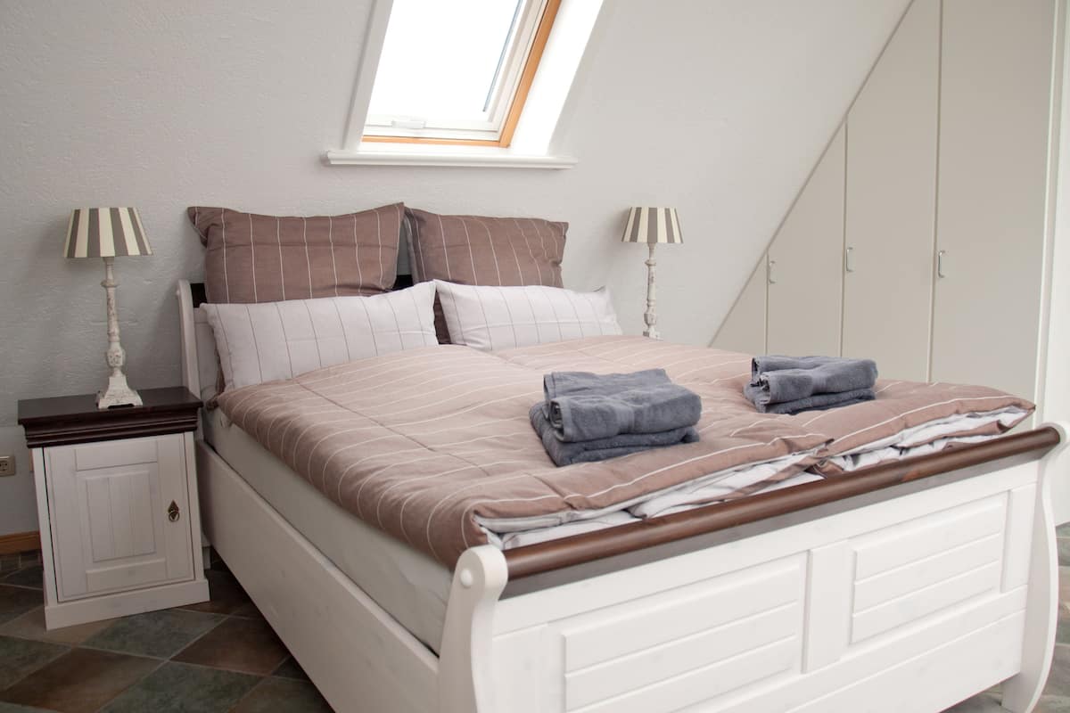 A bedroom with a bed, two nightstands, a wardrobe, and a skylight.