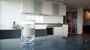 A modern kitchen with white cabinets, a stainless steel oven, and a dining area with a glass table. - urlaubsart - Guldehof (Stoltebuell)