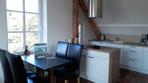 A modern kitchen with a dining area, featuring a large window, wooden beams, and a stainless steel range hood. - urlaubsart - Am Rathaus (Kappeln)