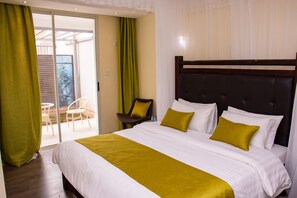 Quarto de hotel com uma cama grande, uma cadeira, uma mesa pequena e uma porta de vidro deslizante para uma varanda.