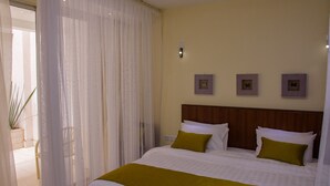 A hotel room with a bed, white curtains, a wooden headboard, and three framed pictures on the wall. - Nairobi Executive Suites (Syokimau)