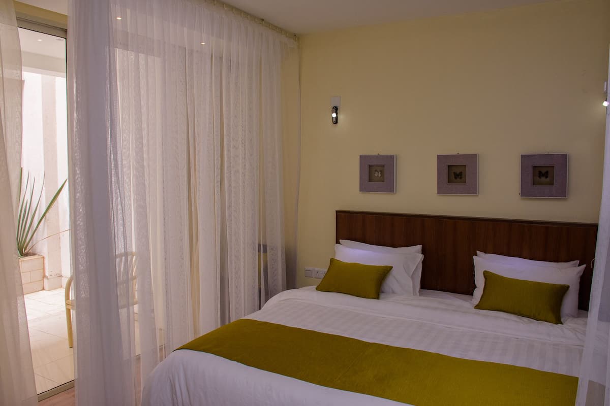 Ein Hotelzimmer mit einem Bett, weißen Vorhängen, einem hölzernen Kopfteil und drei gerahmten Bildern an der Wand.