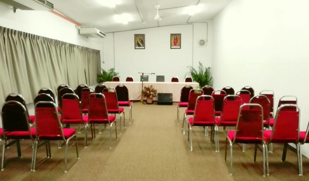 A conference room with rows of red chairs facing a long table with a white tablecloth.