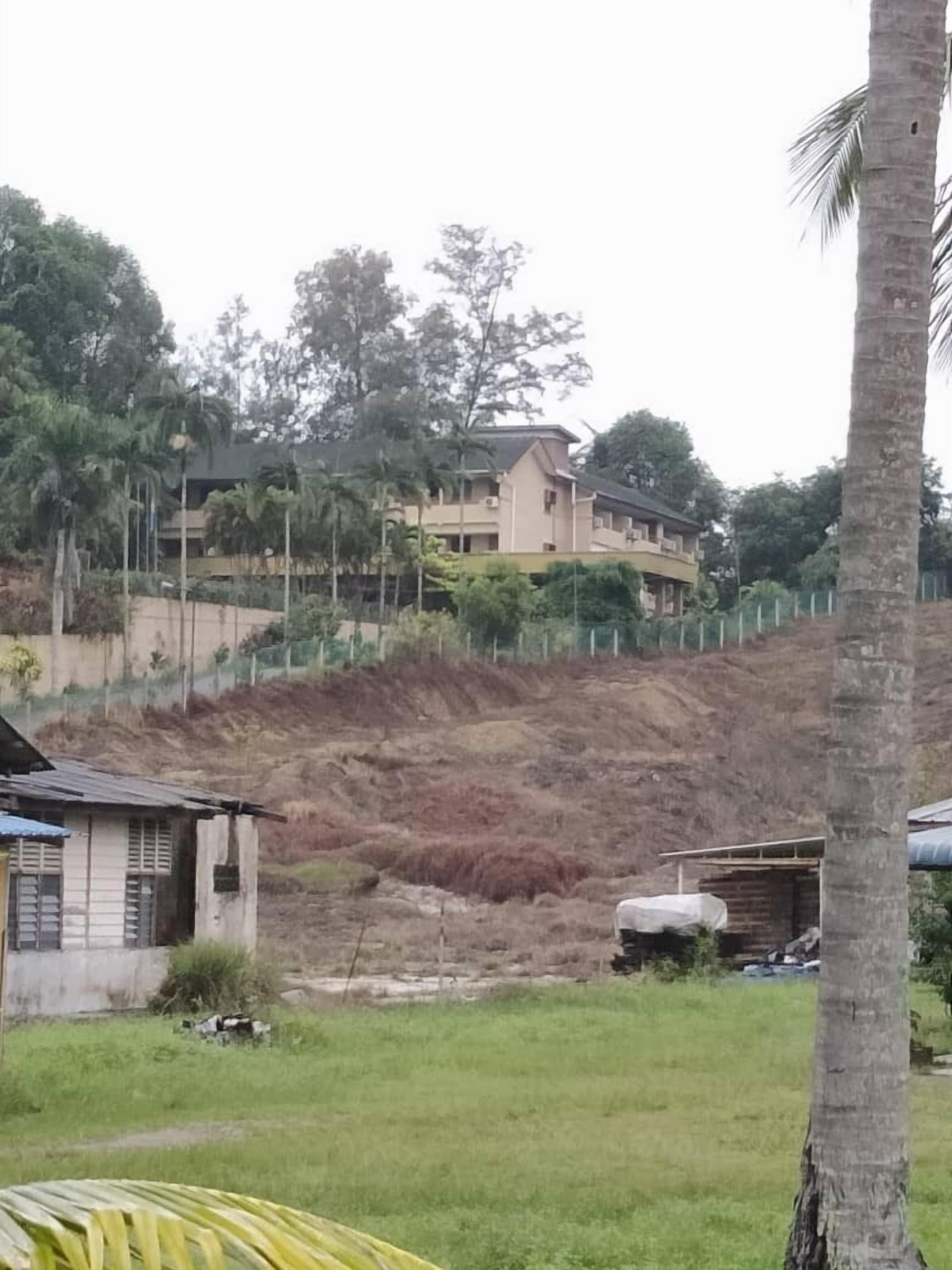 Una zona residencial con una casa en una colina, un edificio pequeño en primer plano y una palmera.