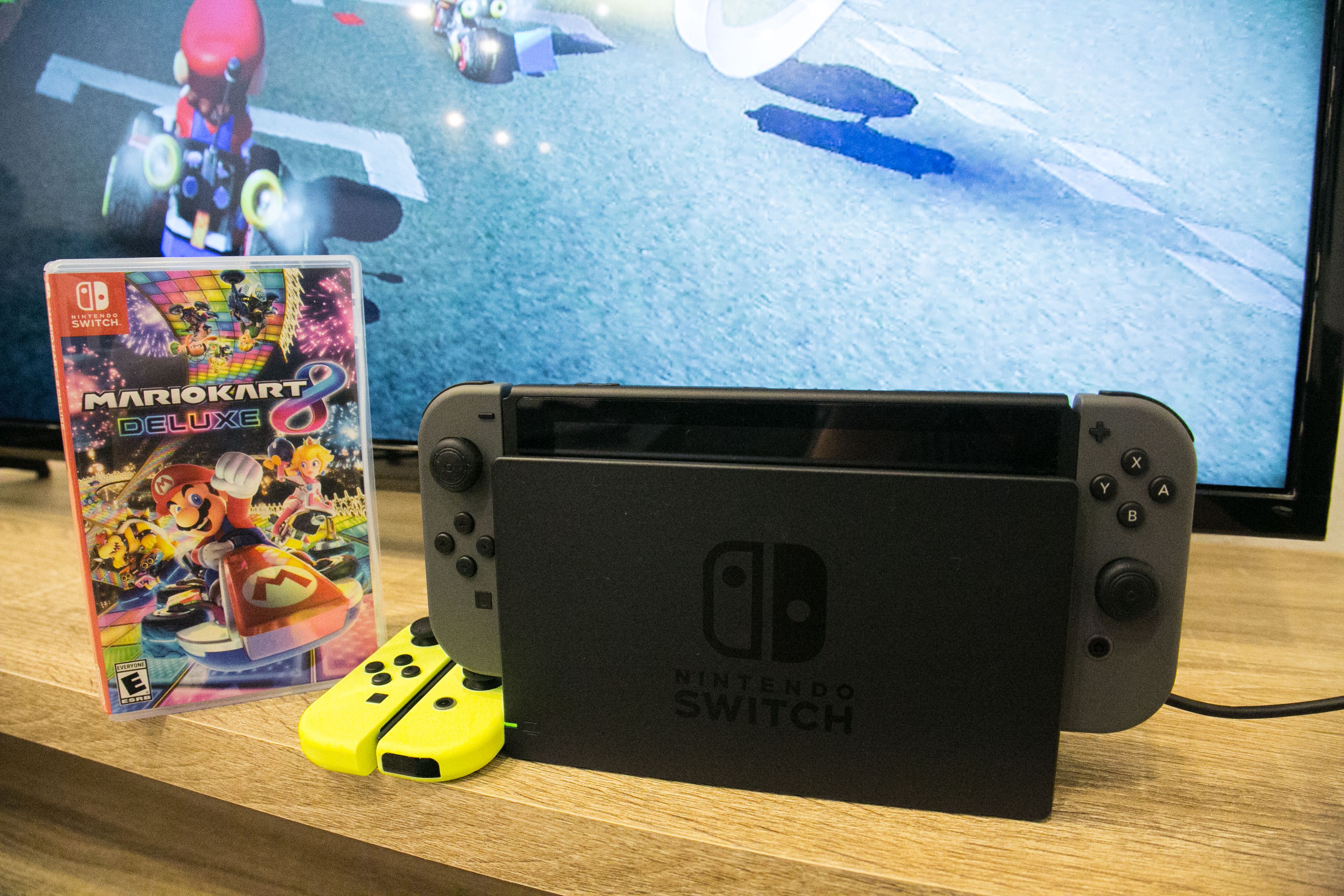 Een Nintendo Switch console op een houten oppervlak, met Mario Kart 8 Deluxe en een controller ernaast.