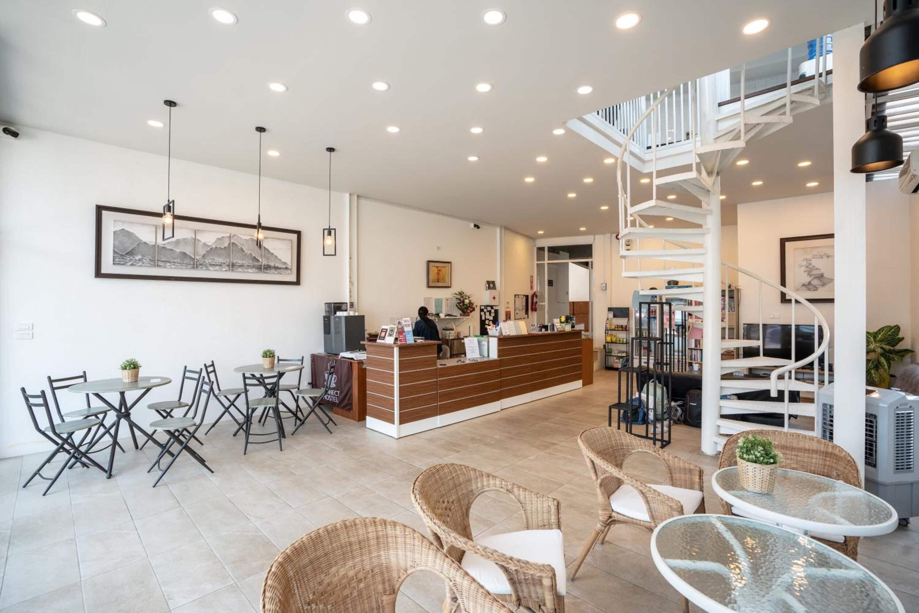 A modern hotel lobby with a reception desk, wicker furniture, and a spiral staircase.
