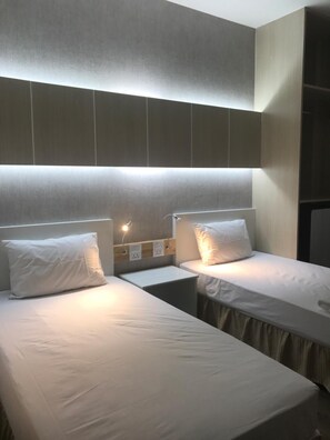 A hotel room with two single beds, each with a pillow and a bedside table.