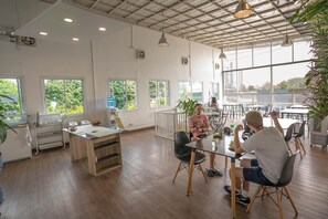 A spacious indoor area with large windows, a wooden floor, and a table where people are seated.