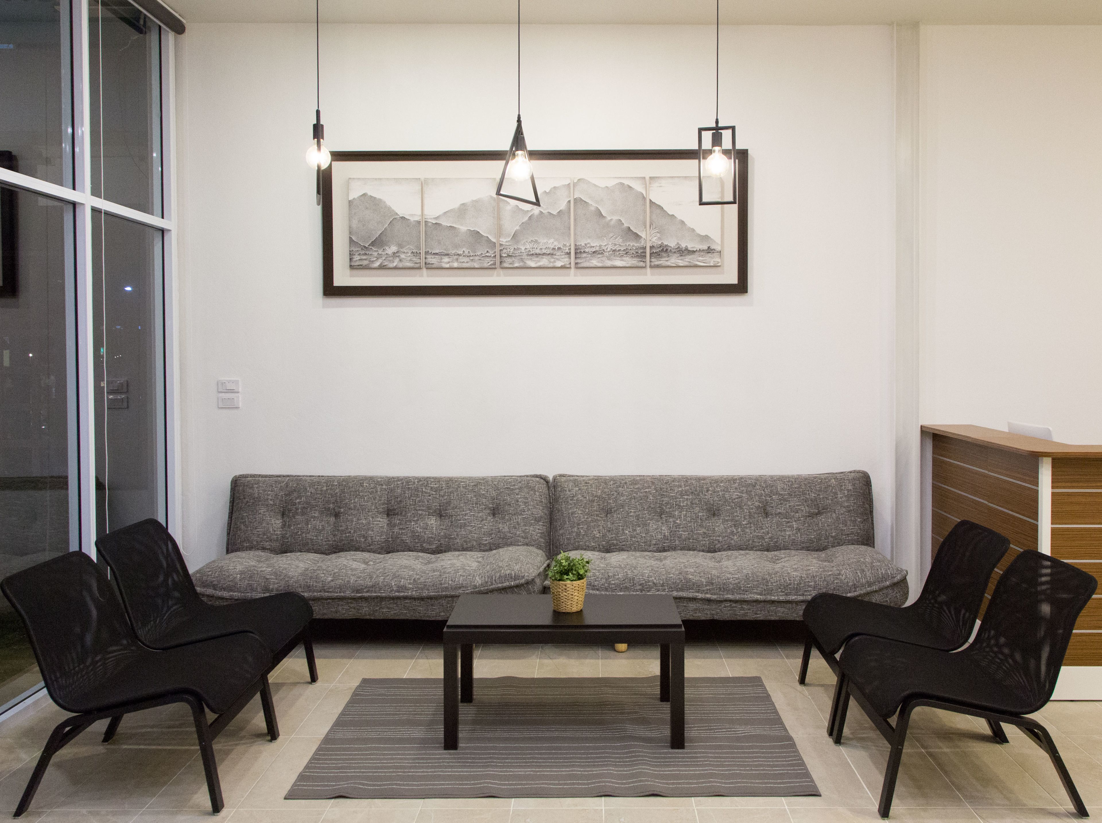 Un salon moderne avec un canapé gris, deux fauteuils noirs, une table basse noire et un tableau encadré représentant des montagnes accroché au mur.