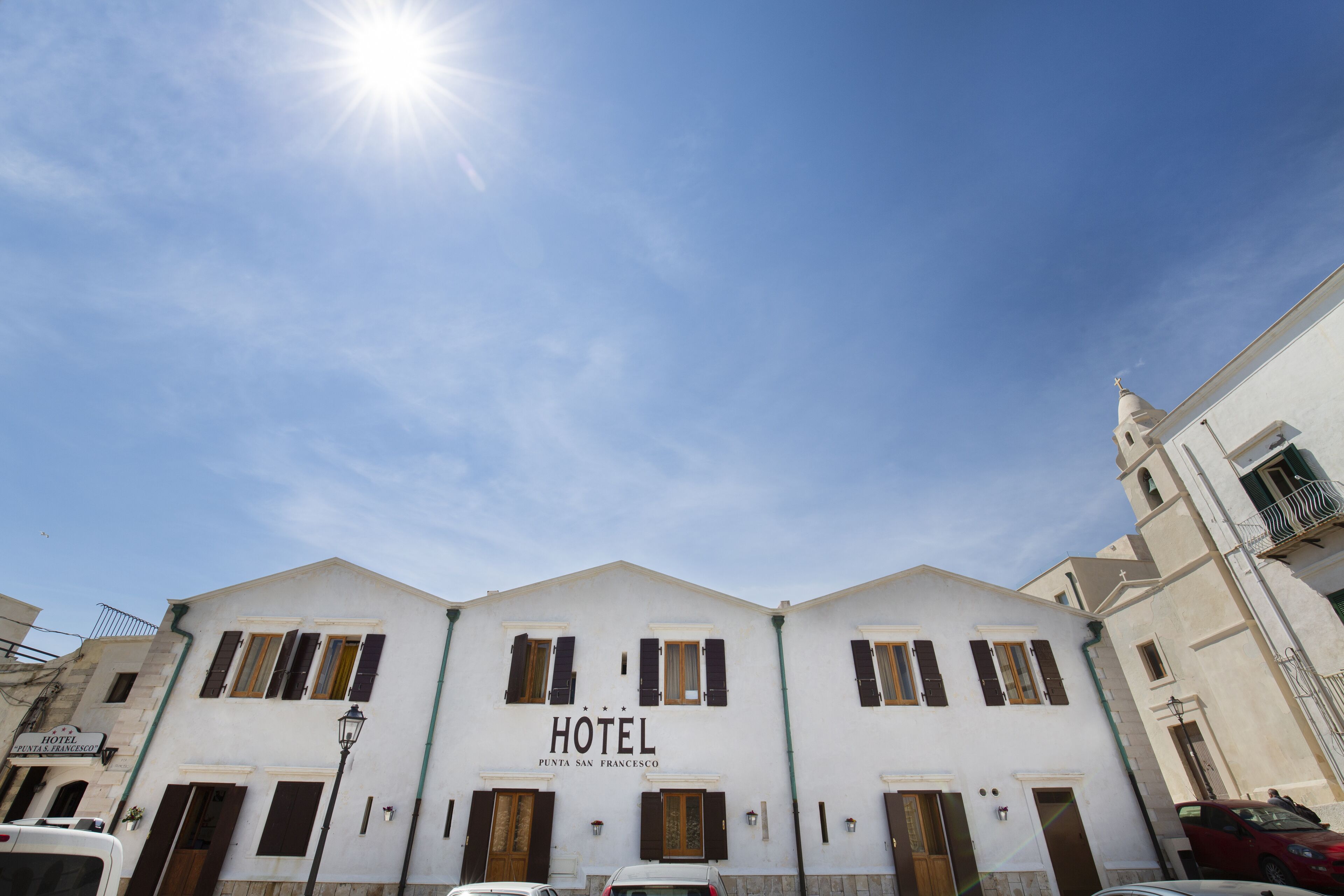 Een wit gebouw met het bord "HOTEL PUNTA SAN FRANCESCO" en meerdere ramen met luiken.