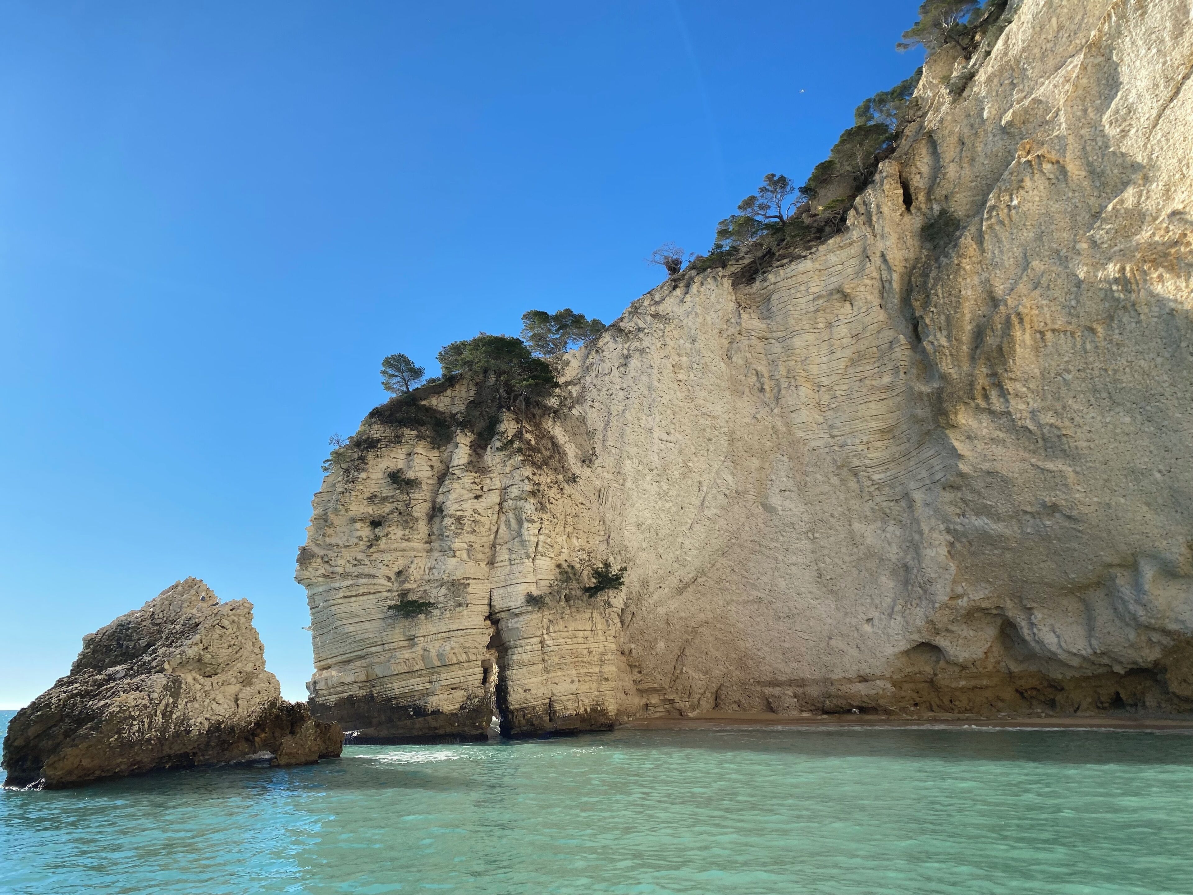 A coastal cliff with clear water and a rock formation.