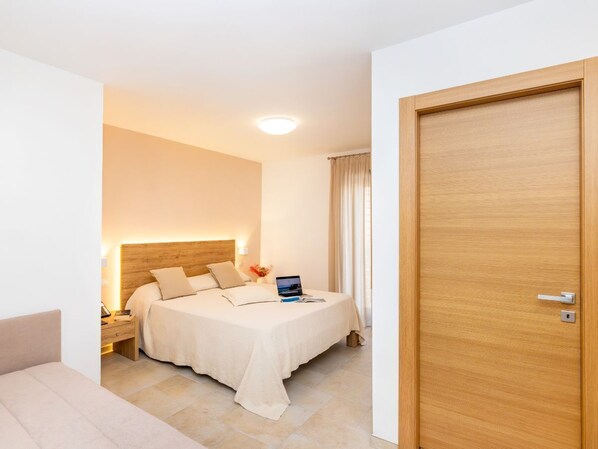 A hotel room with a bed, bedside table, lamp, and a wooden door. - Hotel Punta San Francesco (Vieste)