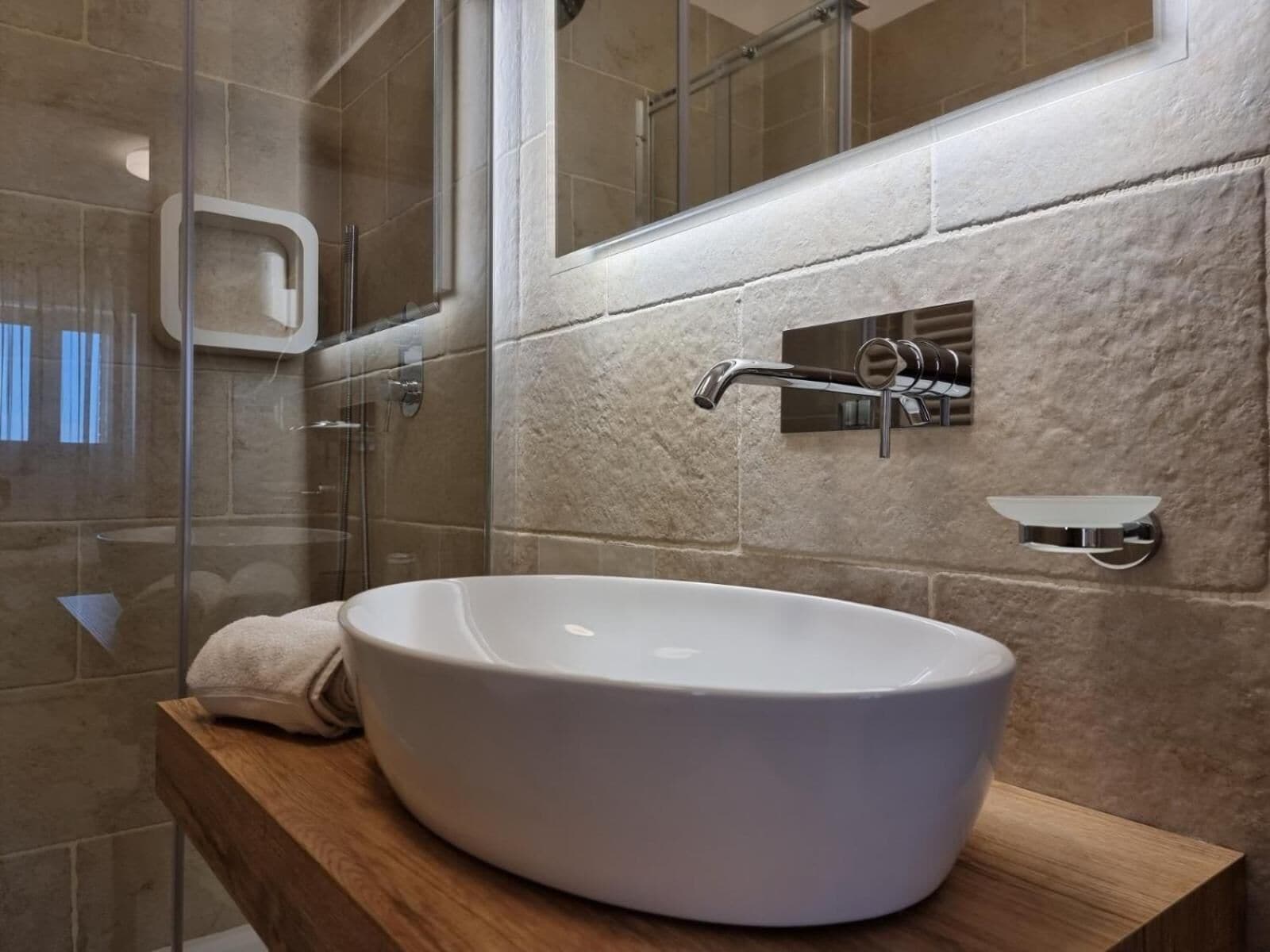 A bathroom with a large white vessel sink, a glass shower enclosure, and a wooden vanity.