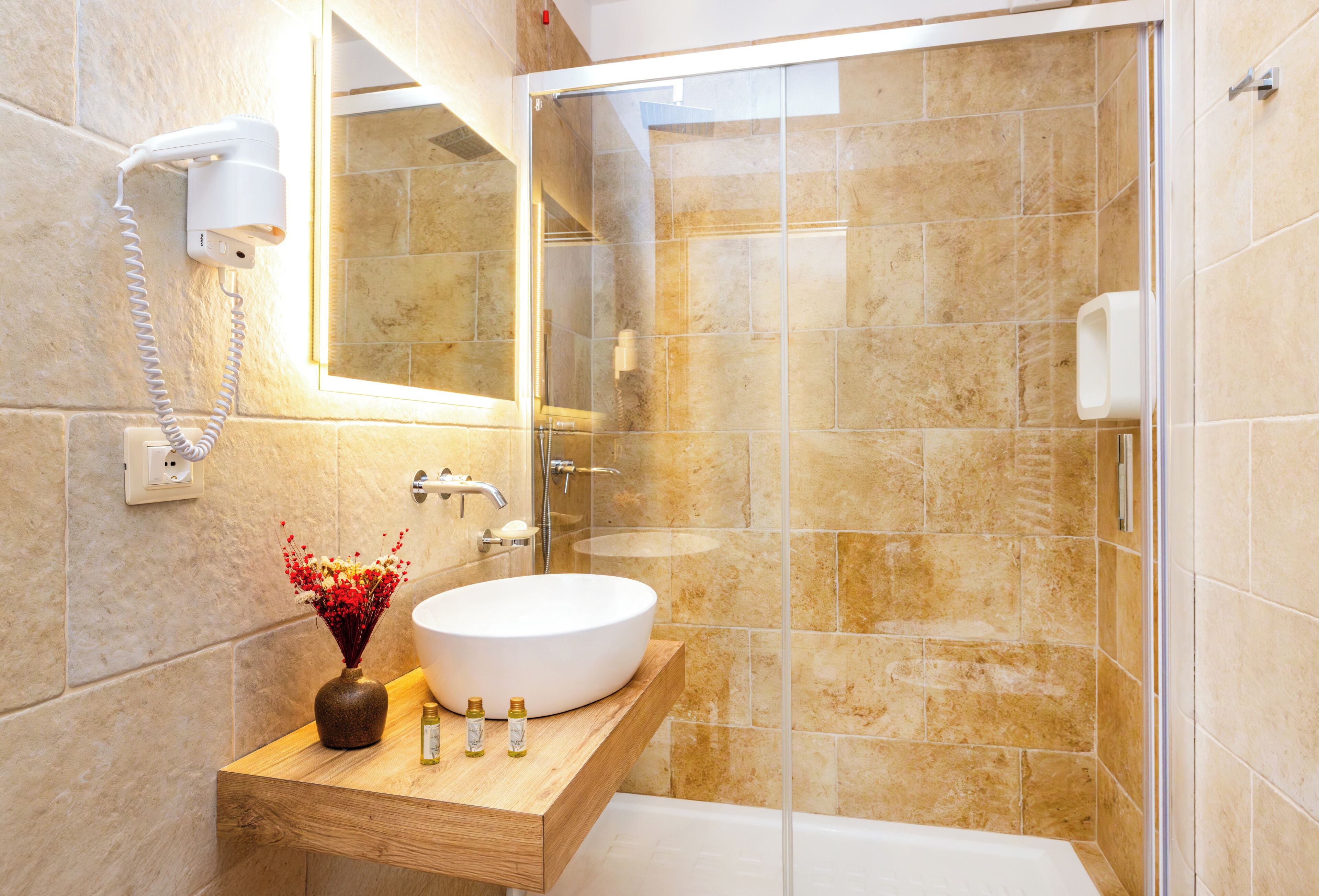 Un baño con un lavamanos blanco, un mueble de tocador de madera, una cabina de ducha de vidrio y un espejo.