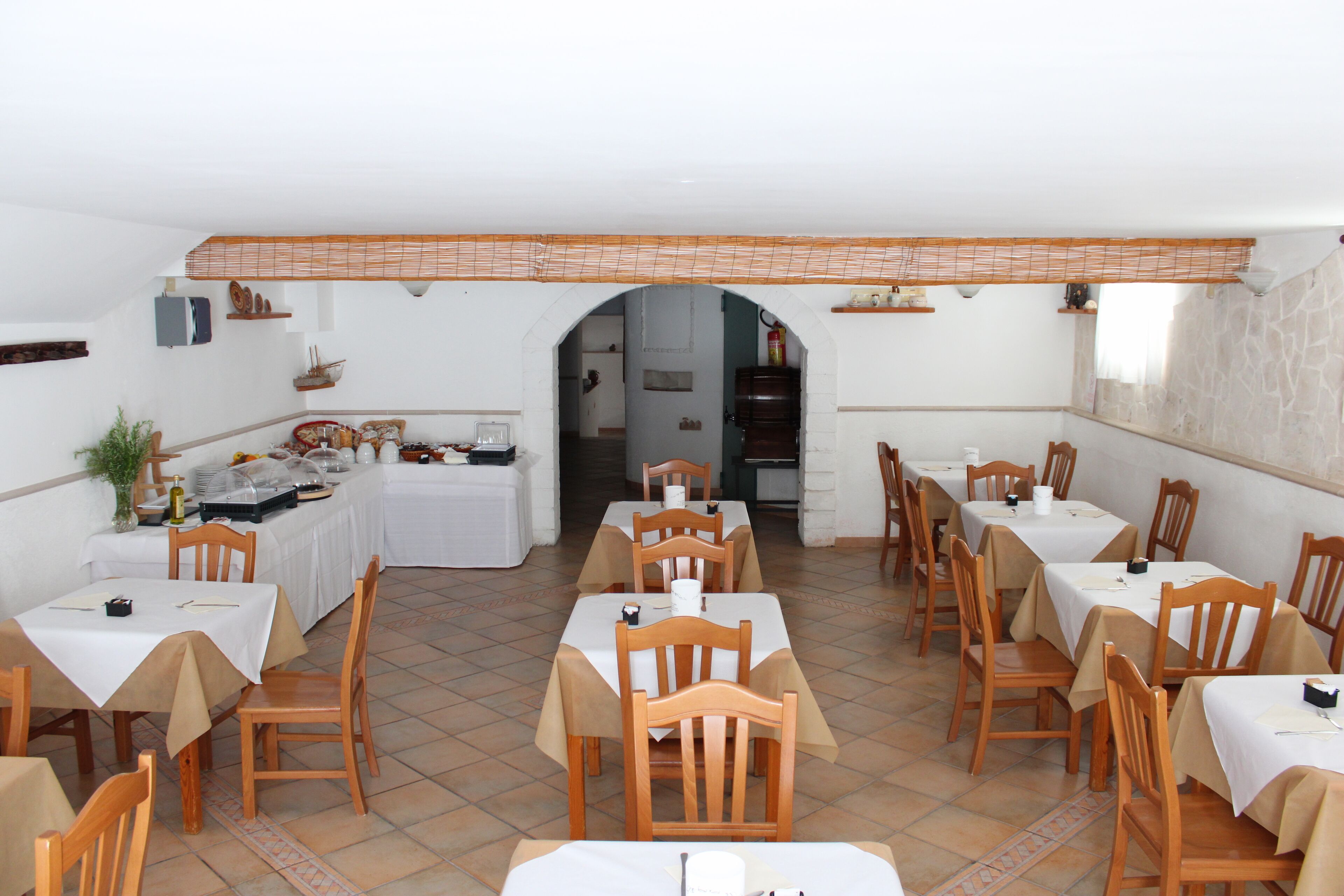 A dining area with multiple tables and chairs, a kitchen area in the background, and a tiled floor.