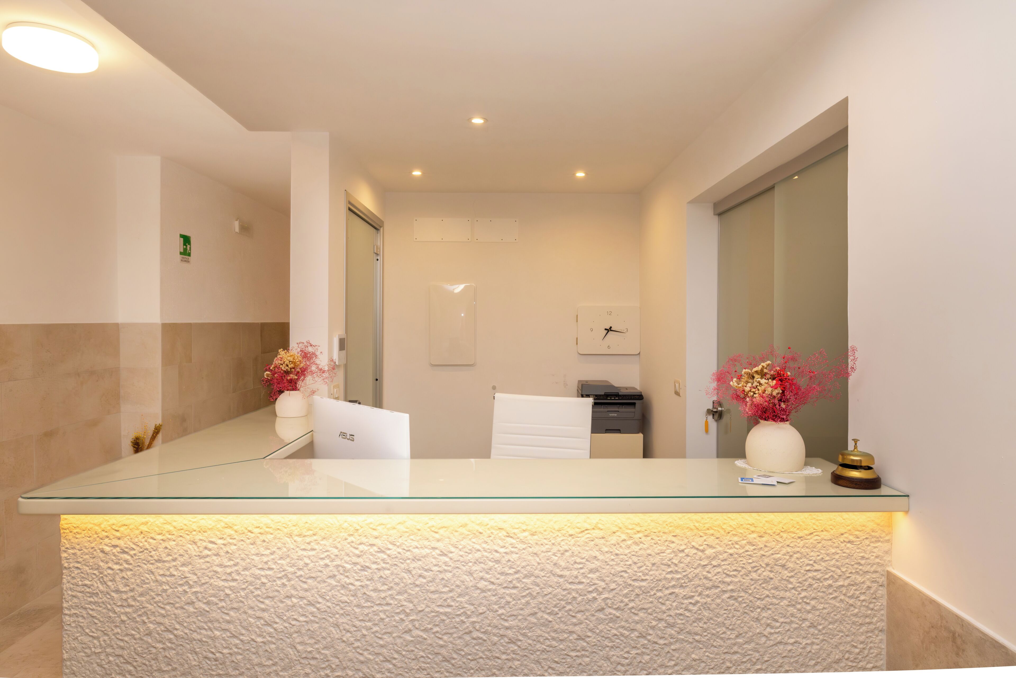 A reception desk with a glass top, a white towel, a clock, and a vase with flowers.