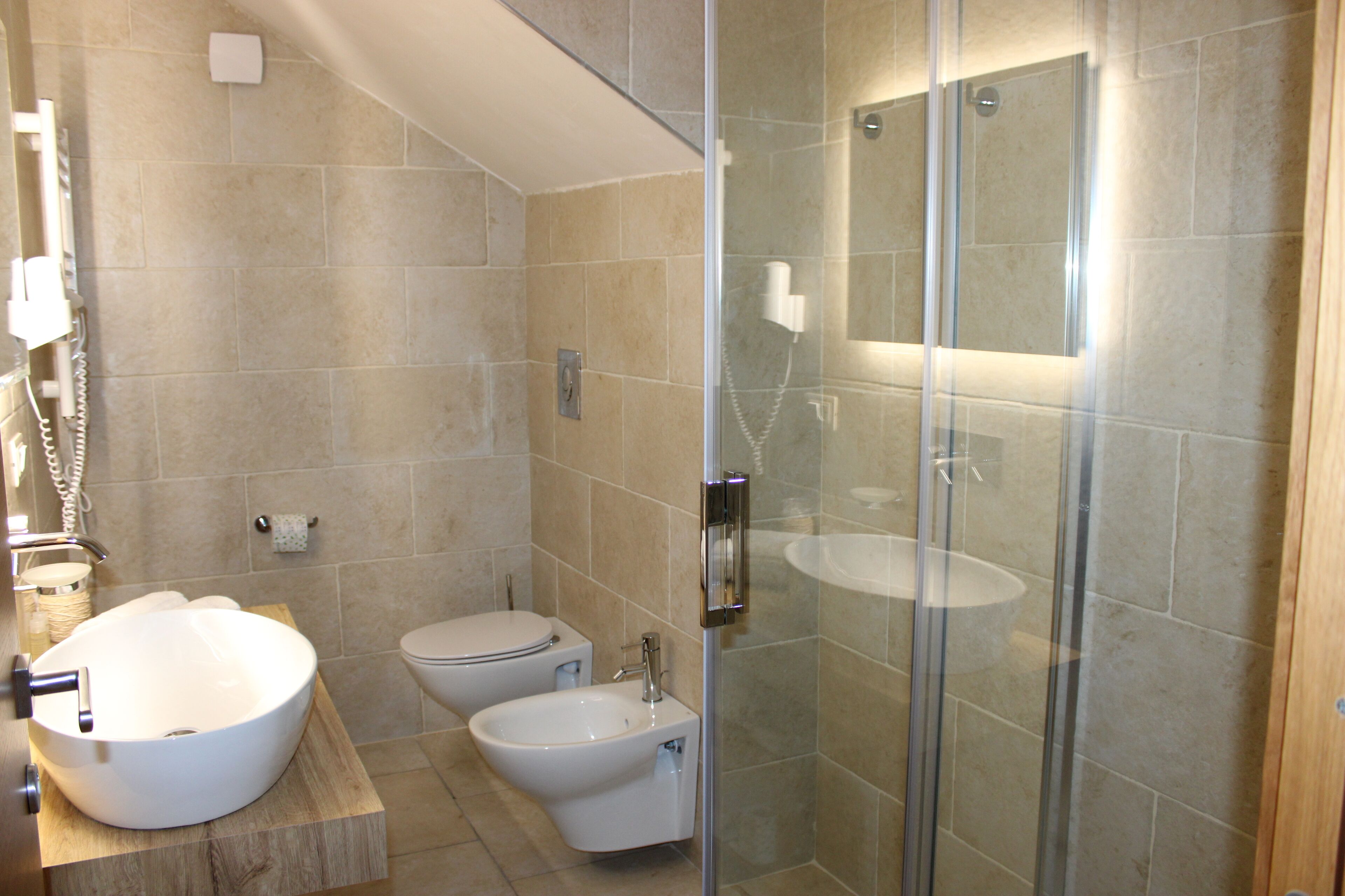 A modern bathroom with a large vessel sink, a bidet, a toilet, and a glass-enclosed shower area.