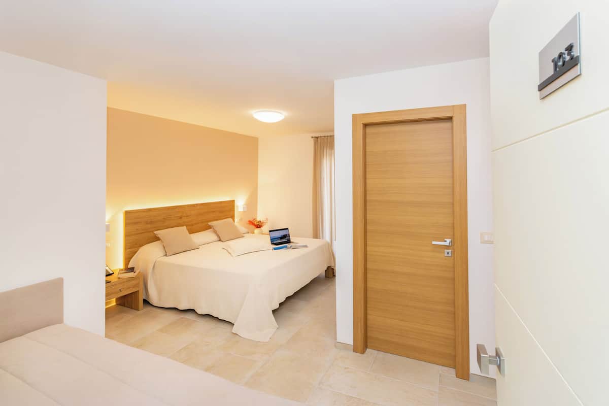 Una habitación de hotel con cama, mesita de noche, lámpara y una puerta.