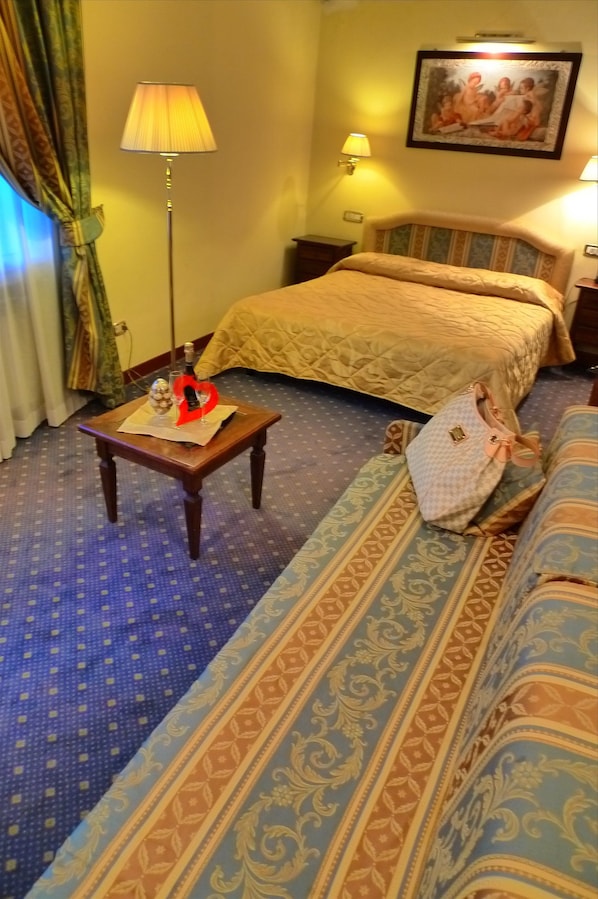 A hotel room with a bed, a sofa, a small table with a lamp, and a decorative item on the table.