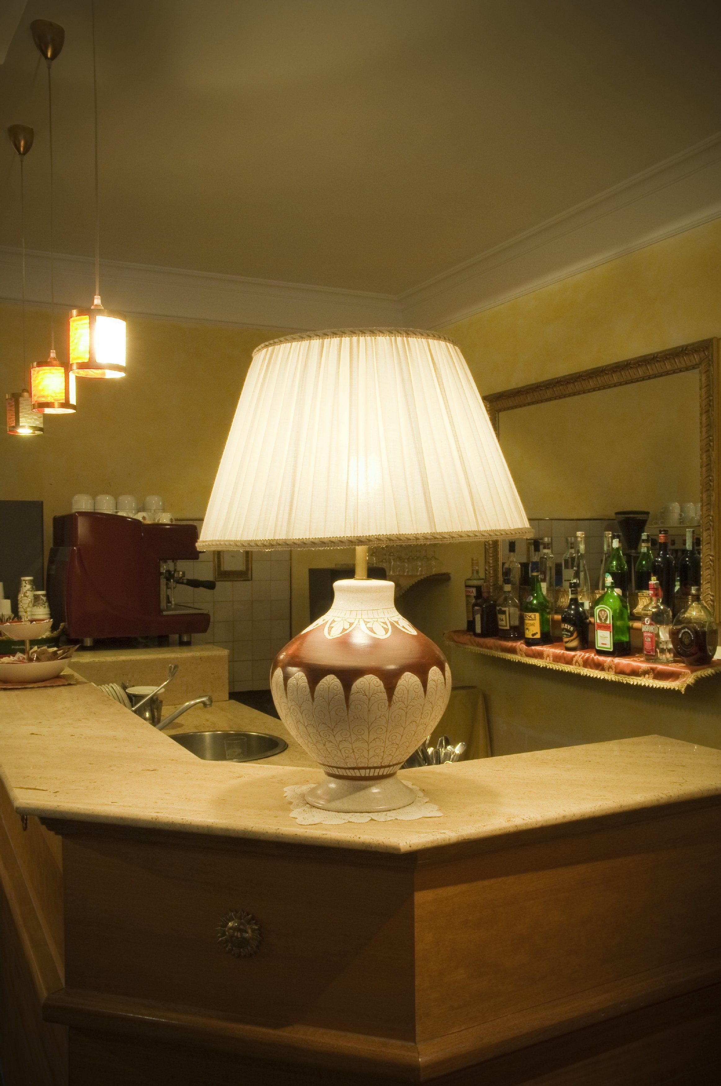 Una zona de bar con una lámpara decorativa, una máquina de café y diversas botellas sobre el mostrador.