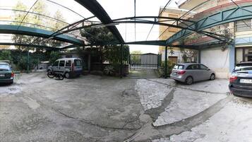 A parking area with a green canopy structure, a gated entrance, and a building with a curved facade in the background.