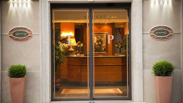 A hotel entrance with a reception desk, a reception sign, and two potted plants.