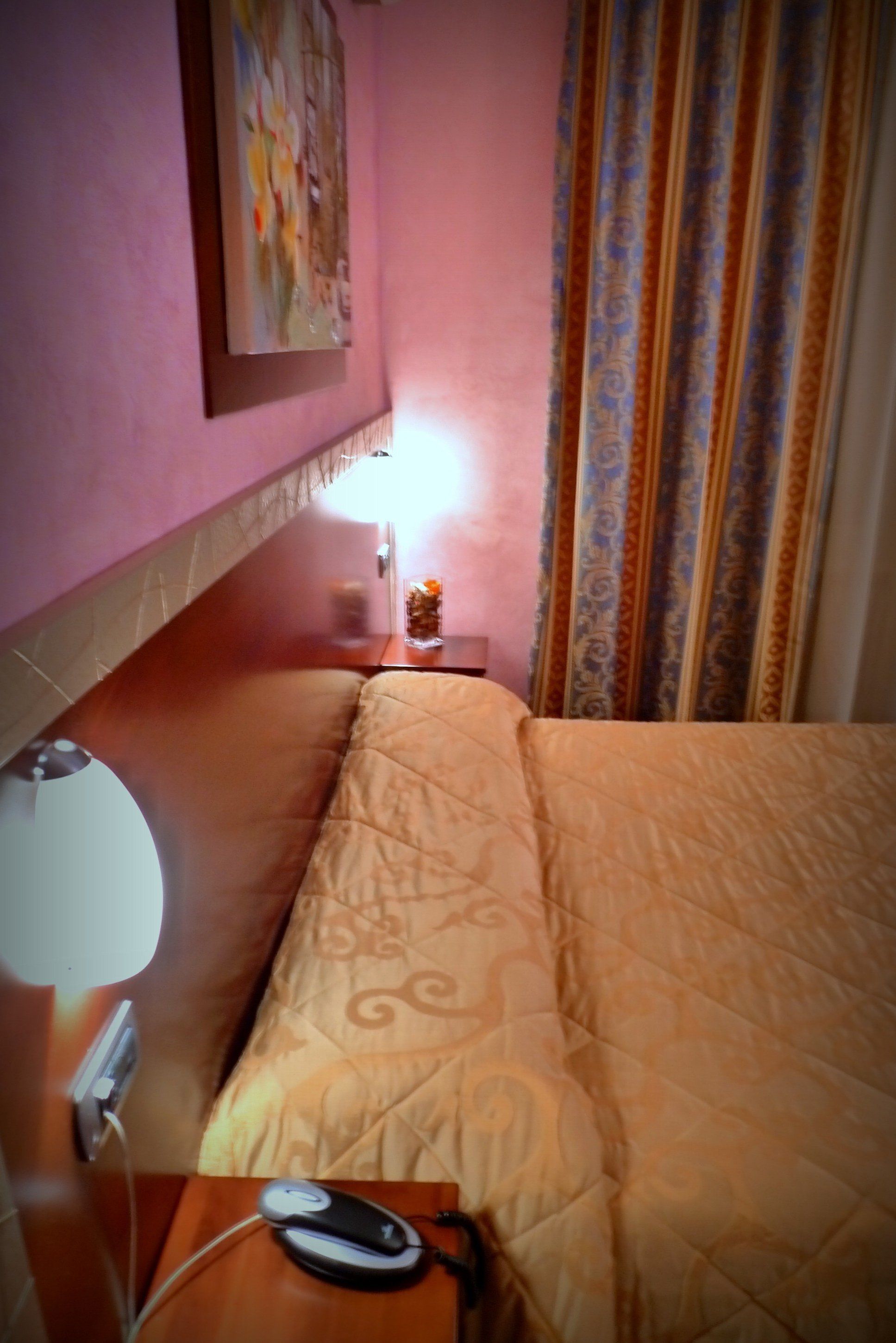 Una habitación de hotel con una cama, una mesita de noche con una lámpara, un ratón de ordenador y un cuadro en la pared.