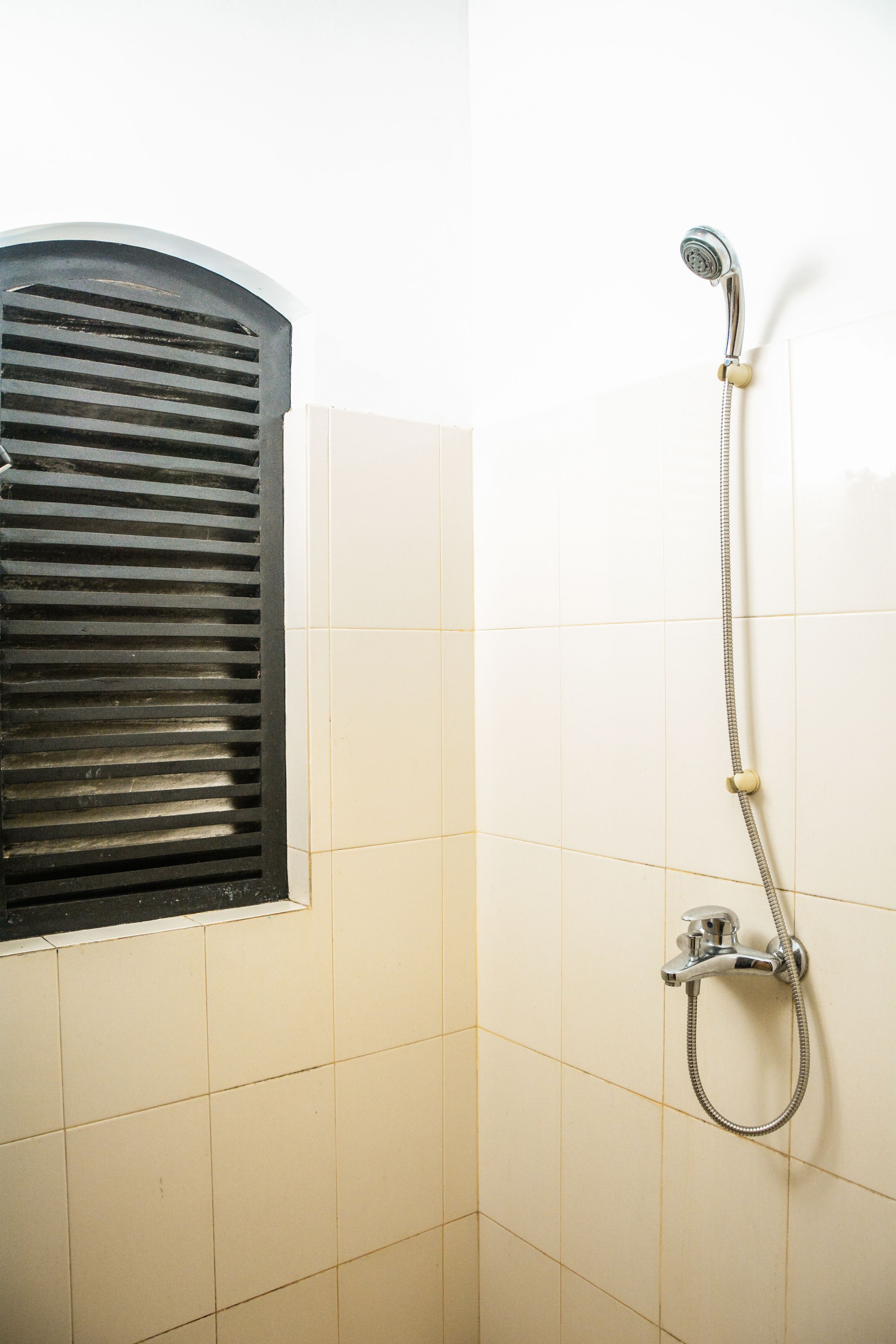 Un baño con ducha, una ventana con persianas y paredes de azulejos.