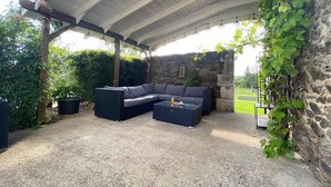An outdoor patio with a stone wall, a black wicker sofa, and a small table. - The Alpaca B&B (Chalais)