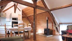 A cozy attic room with a dining area, a sofa, a red rug, and a wood-burning stove. - The Alpaca B&B (Chalais)