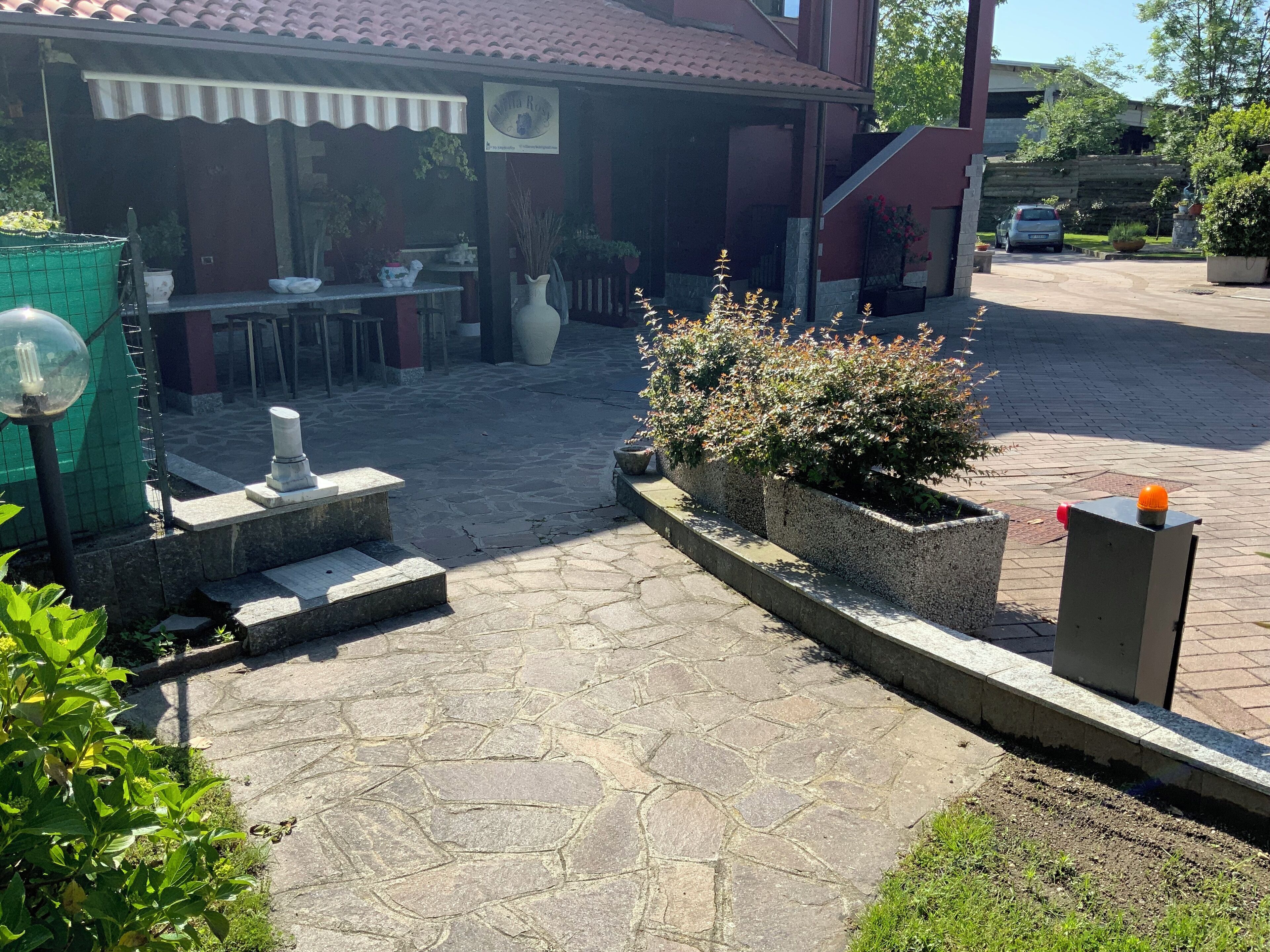 Ein Innenhof mit Steinpflasterung, Gartenmöbeln, Topfpflanzen und einem Schild mit der Aufschrift 'Villa Rosa'.