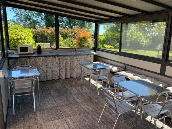 A covered patio area with a kitchen counter, seating, and a view of the garden. - Villa Rosy B&B (Paruzzaro)