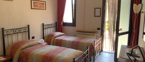 A bedroom with two beds, a radiator, a window with curtains, and a door leading outside.