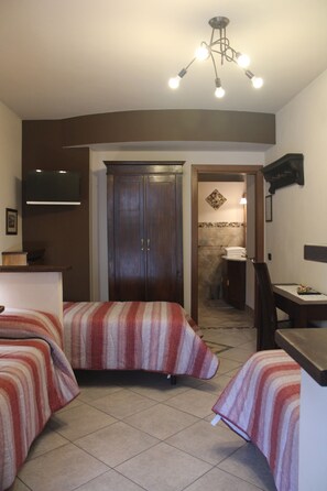 A hotel room with two beds, a wardrobe, a television, and a bathroom visible through an open door. - Villa Rosy B&B (Paruzzaro)