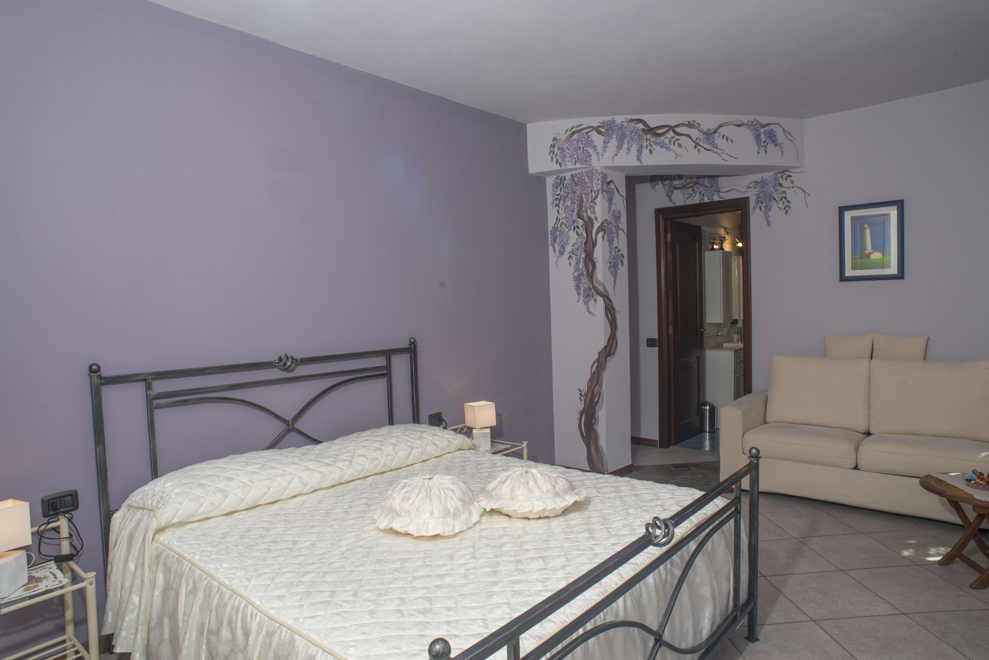 A bedroom with a bed, bedside table, lamp, and a sofa.