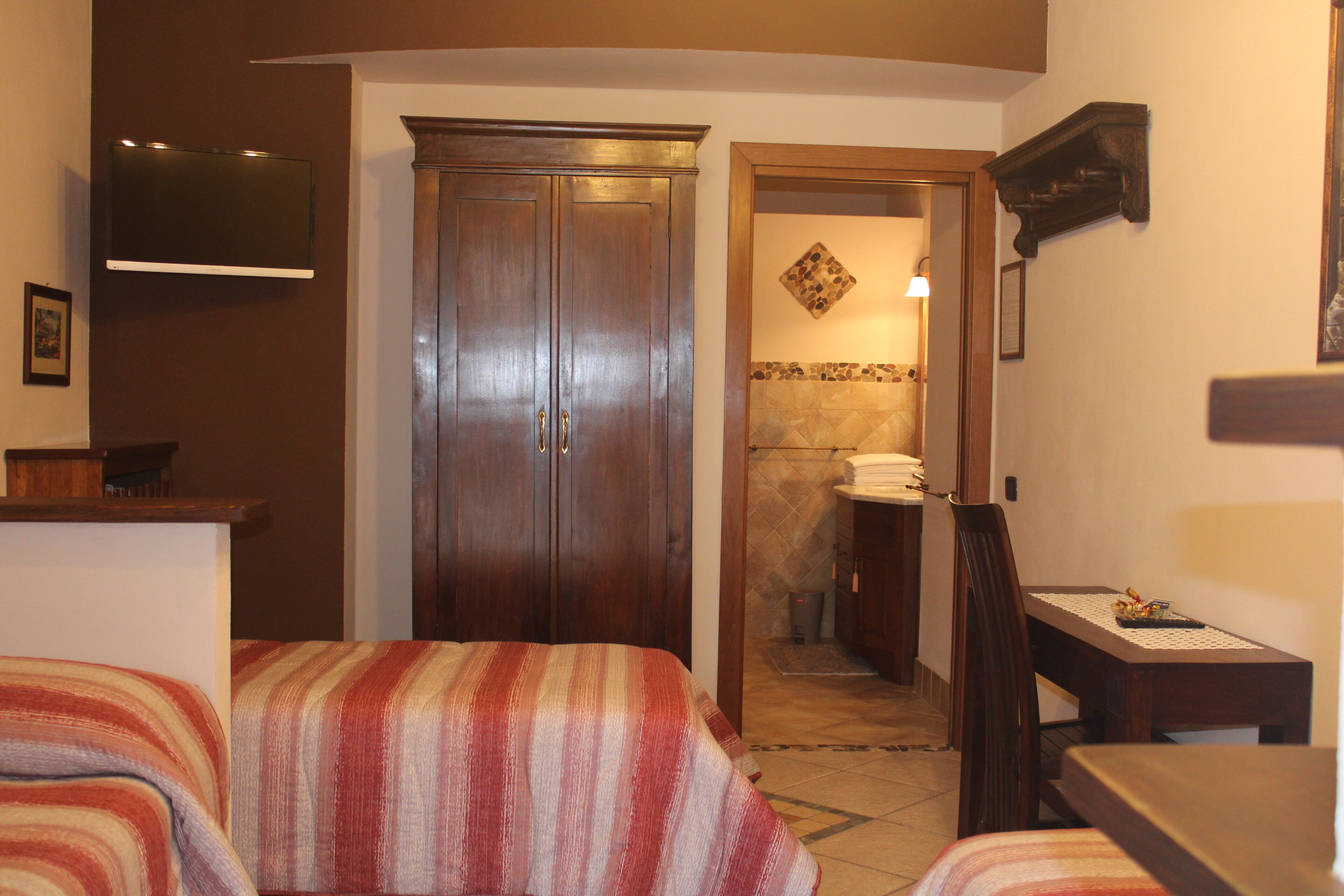 A hotel room with a bed, a desk, a TV mounted on the wall, and a bathroom visible through an open door.