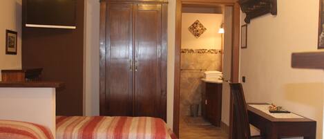 A hotel room with a bed, a desk, a TV mounted on the wall, and a bathroom visible through an open door.