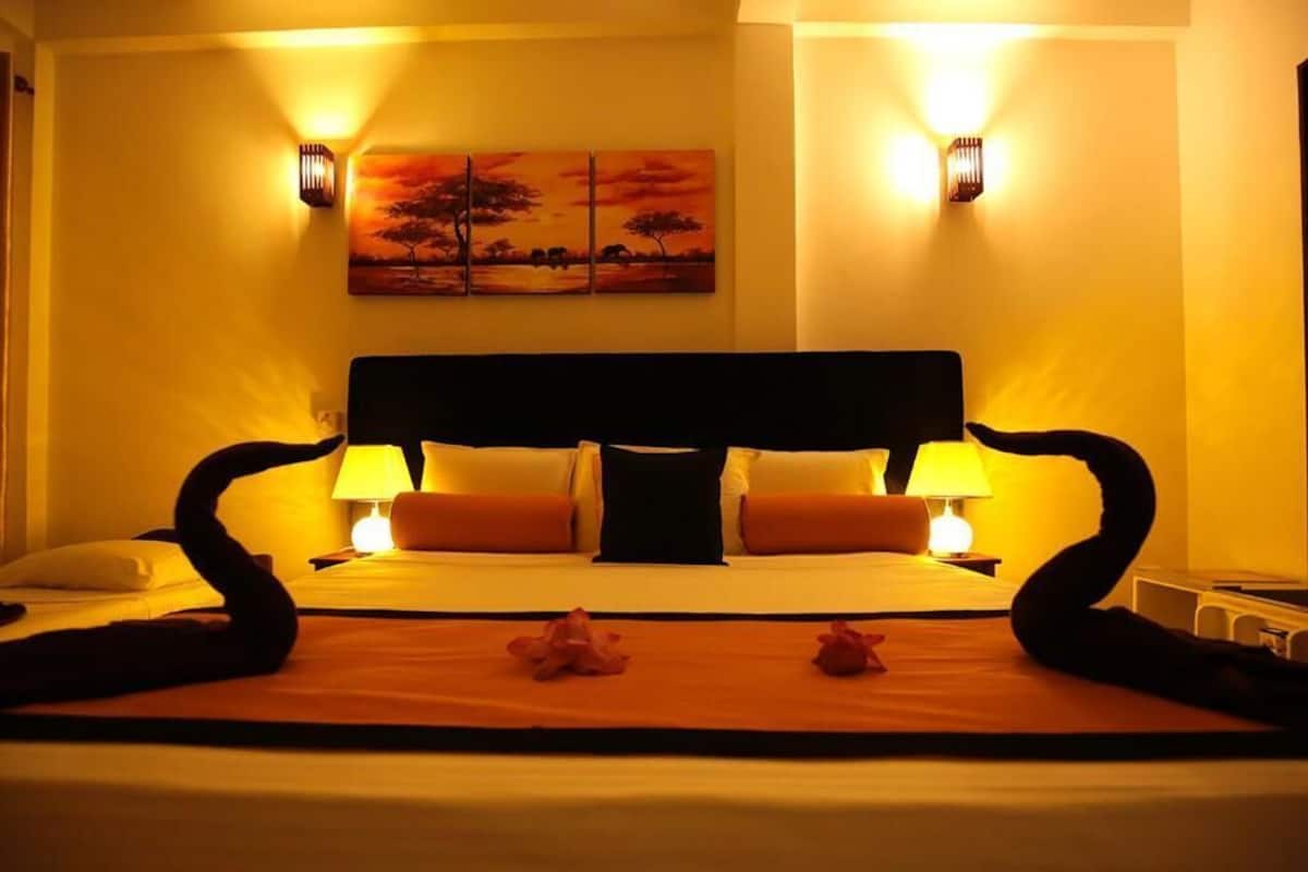 A hotel room with a large bed, two bedside lamps, a painting on the wall, and a decorative arrangement of flowers on the bed.