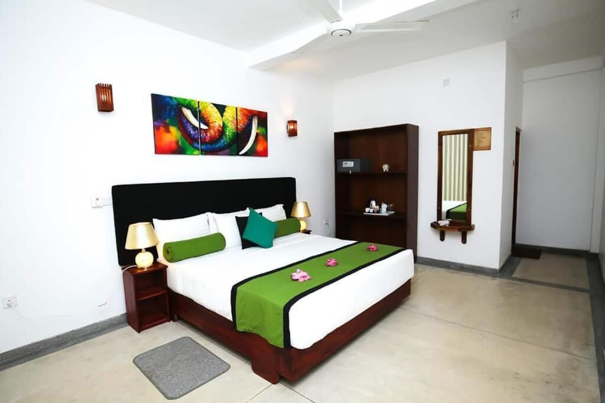 A bedroom with a bed, bedside lamps, a nightstand, a green throw blanket, a colorful abstract painting, a wooden wardrobe, and a mirror.